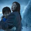 Cena icônica de A Grande Inundação (Netflix 2025) com mãe (Kim Da-mi) carregando filho no colo enquanto onda gigante apocalíptica ameaça ao fundo no final do filme.