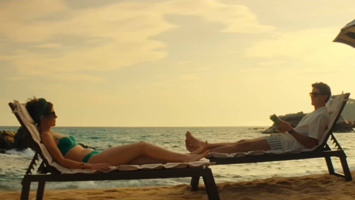Cena do filme De Férias com Você na Netflix mostra Poppy e Alex relaxando na praia durante uma viagem marcante