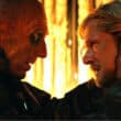 Cena intensa de Extermínio: O Templo dos Ossos (2026) com um homem careca encarando um jovem loiro em ambiente iluminado por fogo.