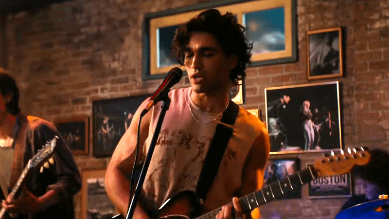 Justin em cena de Off Campus revelando segredos sobre música de Hannah